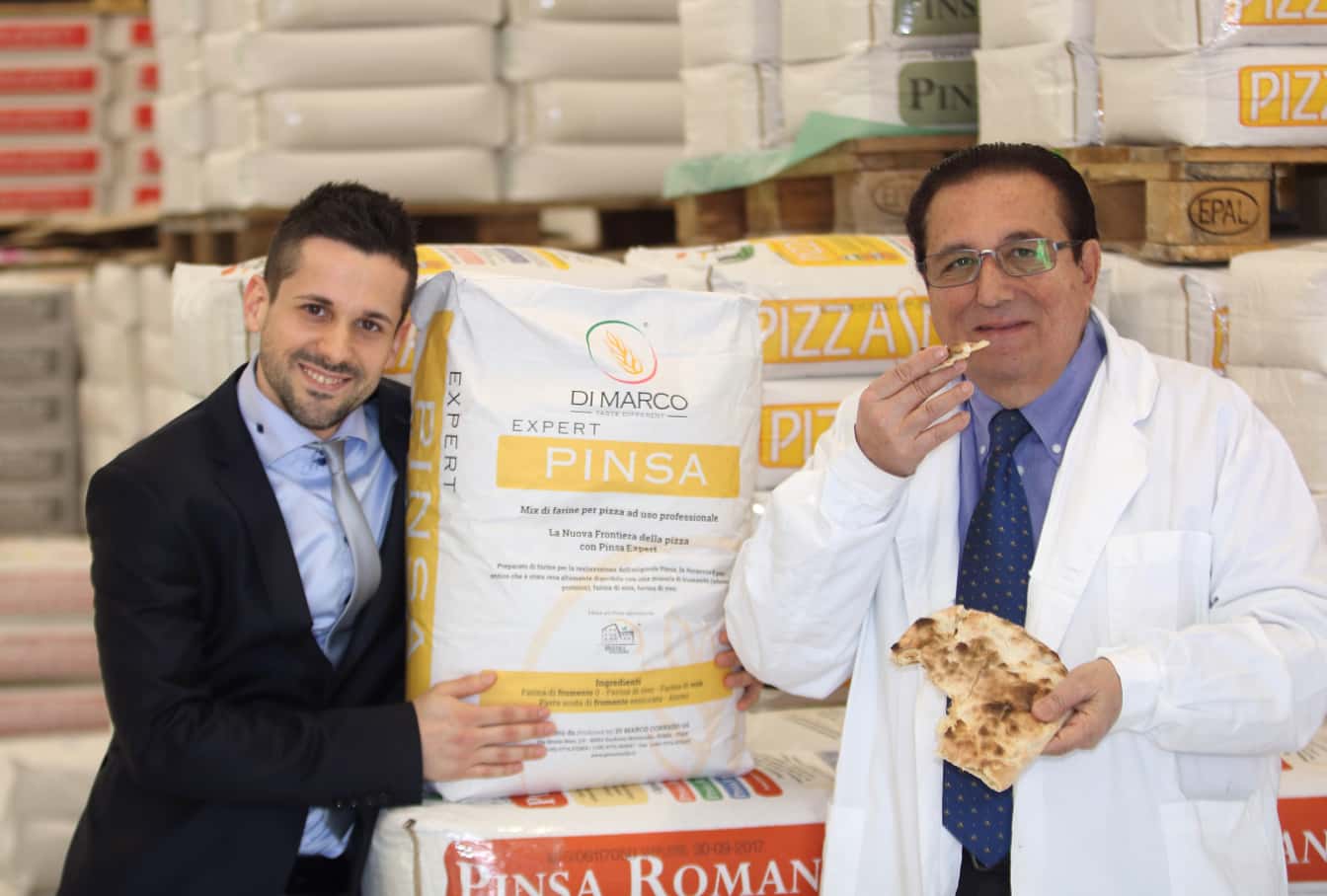 Foto di Corrado Di Marco mentre assaggia un impasto di Pinsa e di un altro membro dello staff con dei sacchi di farina alle loro spalle.